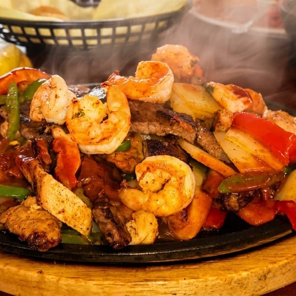 Sizzling fajitas with shrimp, steak, chicken, and colorful peppers on a cast iron skillet.